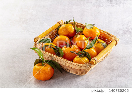 Fresh tangerines with green leaves in woven basket on light gray surface Fresh tangerines with green leaves in woven basket on light gray surface 140780206
