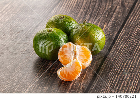 Green tangerines with peeled segments on dark wood surface Green tangerines with peeled segments on dark wood surface 140780221