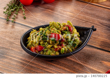 Guacamole with red peppers in black bowl on wooden table Guacamole with red peppers in black bowl on wooden table 140780225