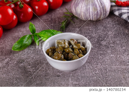 Capers in white bowl with cherry tomatoes basil and garlic on textured surface Capers in white bowl with cherry tomatoes basil and garlic on textured surface 140780234