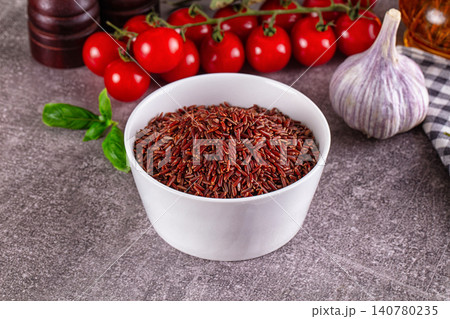 Red rice in white bowl with cherry tomatoes garlic and basil on gray surface 140780235