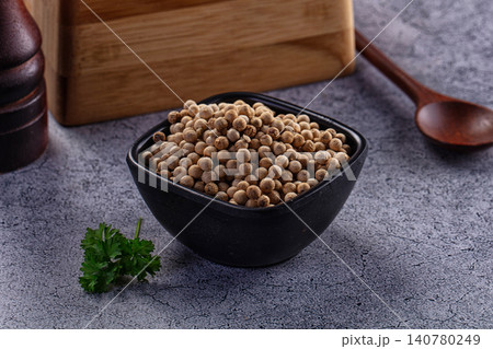 White peppercorns in black bowl with parsley and wooden spoon on gray surface White peppercorns in black bowl with parsley and wooden spoon on gray surface 140780249
