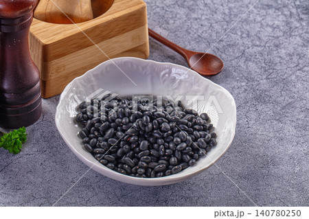 Black beans in white ceramic bowl with wooden spoon and pepper mill on gray textured surface Black beans in white ceramic bowl with wooden spoon and pepper mill on gray textured surface 140780250