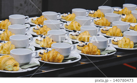 Rows of coffee break sets with croissants and tarts on plates for seminar conference catering. Rows of coffee break sets with croissants and tarts on plates for seminar conference catering. 140780473