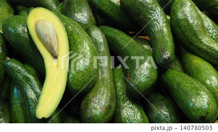 High angle view of fresh green avocados pile with a sliced half showing seed and yellow pulp. High angle view of fresh green avocados pile with a sliced half showing seed and yellow pulp. 140780503