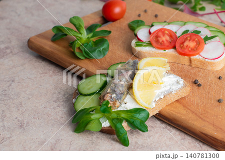 A set of sandwiches with sprats,  homemade curd cream with herbs, with radishes, cucumbers, and tomatoes, on a wooden background. Top view. Copy space. 140781300