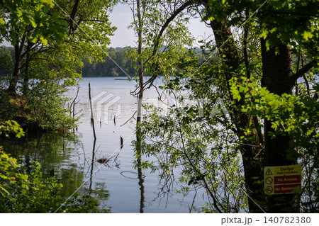 Mercers Lake near Merstham, Surrey, UK. View through trees to the cool waters of the lake. A danger sign is on a tree. 140782380