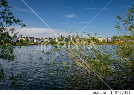 A modern housing development next to the Holmethorpe Lagoons in Mersham, Surrey, UK. Trees in the foreground. Landscape orientation. A modern housing development next to the Holmethorpe Lagoons in Mersham, Surrey, UK. Trees in the foreground. Landscape orientation. 140782391