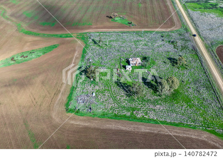 Aerial view of cultivated agricultural fields surrounded by lush green landscape, featuring an old rural cottage and a dirt road leading through the farmland, highlighting the character of the Aerial view of cultivated agricultural fields surrounded by lush green landscape, featuring an old rural cottage and a dirt road leading through the farmland, highlighting the character of the 140782472