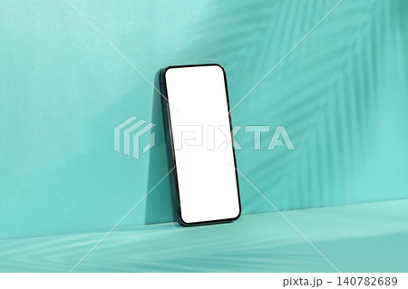 Smartphone mockup with blank screen on mint green background with palm leaf shadow 140782689
