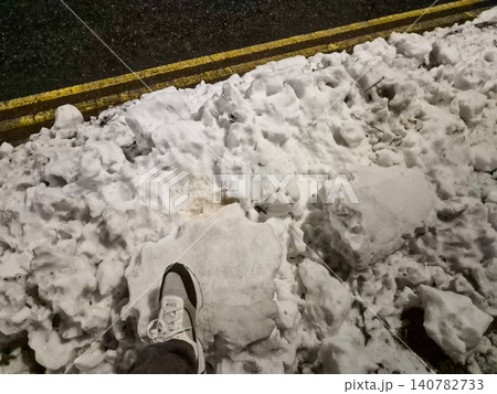 Foot stepping into dirty snow beside roadside curb 140782733