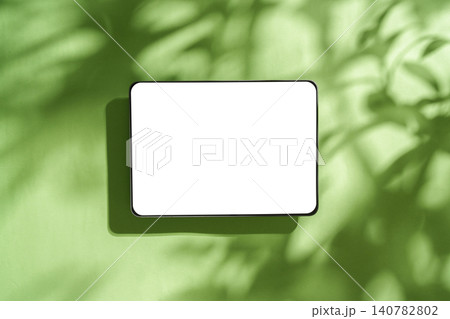 Digital tablet mockup with blank white screen on green background with leaf shadows Digital tablet mockup with blank white screen on green background with leaf shadows 140782802