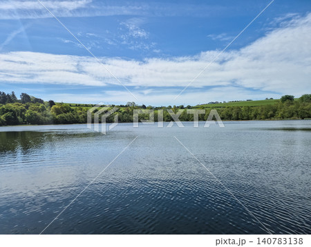 Tranquil lake with blue sky and green shoreline Tranquil lake with blue sky and green shoreline 140783138