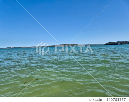 Calm ocean water with distant shoreline and blue sky Calm ocean water with distant shoreline and blue sky 140783377