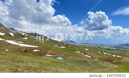 Vast alpine landscape in the highlands of Adjara, Georgia, featuring rolling mountain plateaus, lingering snow patches, dramatic summer clouds and distant Caucasus peaks under a vibrant blue sky. Vast alpine landscape in the highlands of Adjara, Georgia, featuring rolling mountain plateaus, lingering snow patches, dramatic summer clouds and distant Caucasus peaks under a vibrant blue sky. 140783632