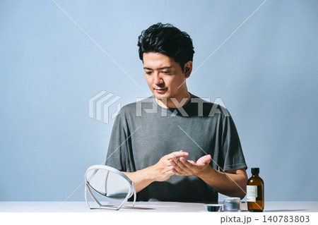 鏡を見ながらクリームを手に取りスキンケアをする30代の日本人男性の美容とメンズビューティーのイメージ 140783803