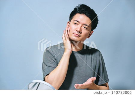 頬に手を当てて肌のケアをする30代の日本人男性の紫外線や日焼け対策の夏イメージ 140783806
