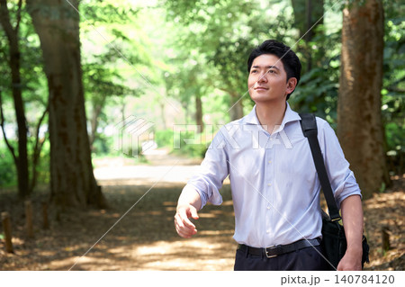 暑い夏に爽やかで緑豊かな公園を笑顔で歩くリラックスした表情の30代の日本人男性の会社員 暑い夏に爽やかで緑豊かな公園を笑顔で歩くリラックスした表情の30代の日本人男性の会社員 140784120