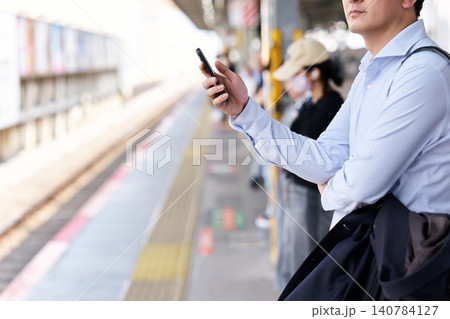 駅のホームでスマートフォンを操作する30代の日本人の男性の会社員の顔無しの匿名イメージ 駅のホームでスマートフォンを操作する30代の日本人の男性の会社員の顔無しの匿名イメージ 140784127