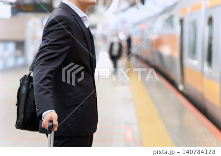 駅のホームでスーツケースを持ち電車を待つ出張中の顔無しの30代から40代の日本人の男性のビジネスマン 駅のホームでスーツケースを持ち電車を待つ出張中の顔無しの30代から40代の日本人の男性のビジネスマン 140784128