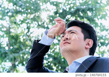 屋外の木の下の木陰で手で日差しを遮る暑くて熱中症になりそうな表情で辛そうな30代の日本人の会社員の男 屋外の木の下の木陰で手で日差しを遮る暑くて熱中症になりそうな表情で辛そうな30代の日本人の会社員の男 140784133