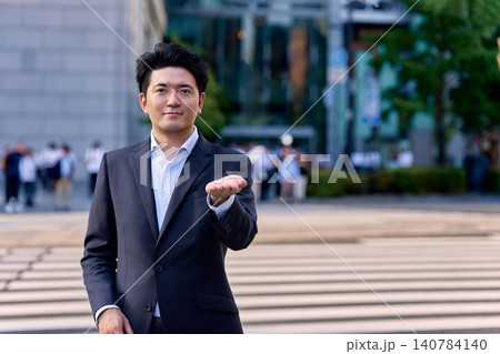 夕方の帰宅ラッシュ時のオフィス街の街中で手の平を上に向けて差し出す30代の日本人の男性のビジネスマン 夕方の帰宅ラッシュ時のオフィス街の街中で手の平を上に向けて差し出す30代の日本人の男性のビジネスマン 140784140
