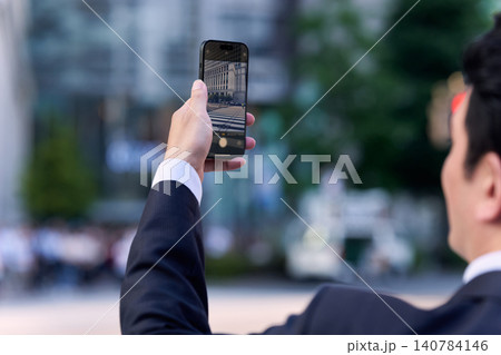 スーツを着た顔無しの日本人の会社員が都会の街並みをスマートフォンで撮影する様子 スーツを着た顔無しの日本人の会社員が都会の街並みをスマートフォンで撮影する様子 140784146