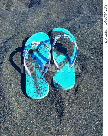Blue flip-flops chill on the black beach of Santorini. 140784235
