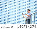 オフィスビルの屋外でスマートフォンを操作する半袖シャツを着た30代の日本人のビジネスマンの男性 140784279