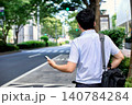 仕事の移動中に通りでスマートフォンのアプリで配車を手配したタクシーを待つ男性の会社員の後ろ姿 140784284