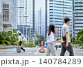 スーツケースを持って都会のビル群立ち並ぶ横断歩道を歩く30代の日本人の男性の会社員と街を行き交う人々 140784289