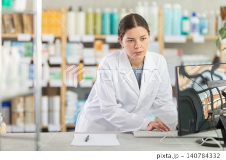 Young female pharmacist working with computer in chemist's shop 140784332