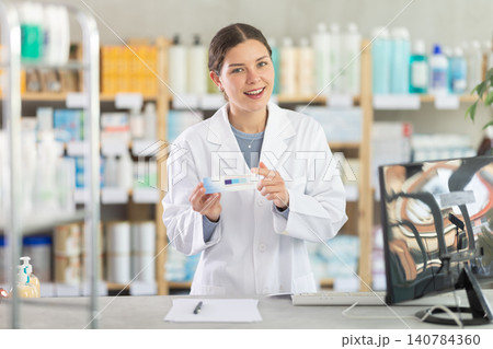 Female pharmacist recommending topical ointment at drugstore counter Female pharmacist recommending topical ointment at drugstore counter 140784360
