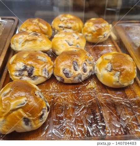 Delicious golden brown buns with whole red beans baked inside, neatly displayed on a rustic wooden tray in a bakery showcase. Traditional Asian sweet pastry, fresh and soft bread for snacking. Delicious golden brown buns with whole red beans baked inside, neatly displayed on a rustic wooden tray in a bakery showcase. Traditional Asian sweet pastry, fresh and soft bread for snacking. 140784483