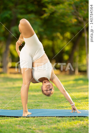 Girl in park on green grass of lawn performs Utthita Hasta Padangushthasana Girl in park on green grass of lawn performs Utthita Hasta Padangushthasana 140784564