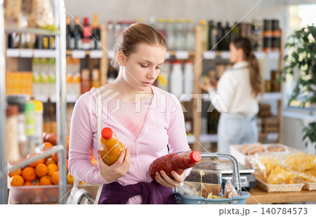 Young girl buyer chooses tomato and peach juices Young girl buyer chooses tomato and peach juices 140784573