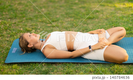 Girl in park on green grass of lawn performs Supta Baddha Konasana Girl in park on green grass of lawn performs Supta Baddha Konasana 140784636