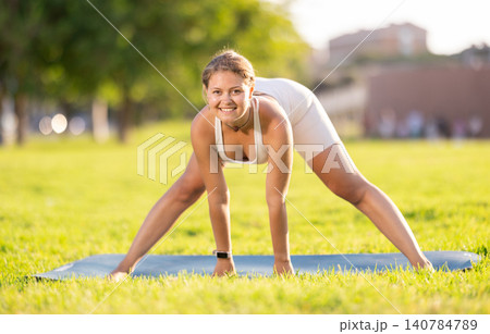 Cheerful girl practicing Prasarita Padottanasana on green summer glade 140784789