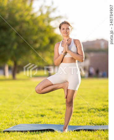 Girl in park on green grass of lawn performs Ardha Baddha Padma Vrikshasana Girl in park on green grass of lawn performs Ardha Baddha Padma Vrikshasana 140784907