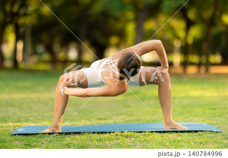 Girl in park on green grass of lawn performs hatha yoga Girl in park on green grass of lawn performs hatha yoga 140784996
