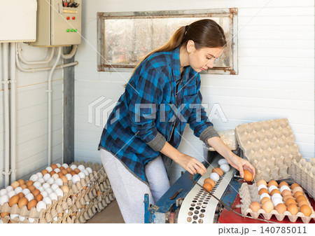 Focused female farmer sorting and packing chicken eggs on farm 140785011