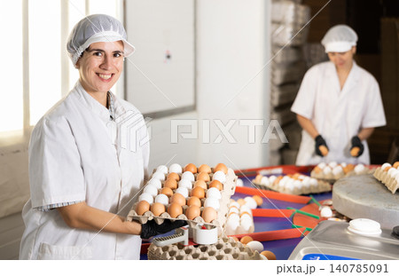 Young Latin female farmer in uniform holding cardboard box full of fresh chicken eggs after sorting and labeling on poultry farm Young Latin female farmer in uniform holding cardboard box full of fresh chicken eggs after sorting and labeling on poultry farm 140785091