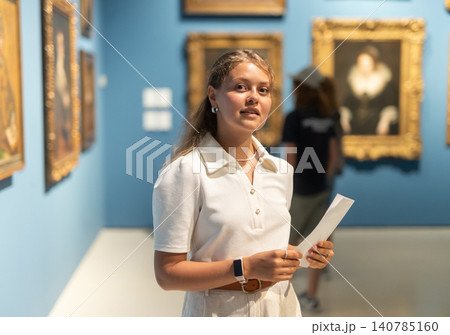 Woman with sheet piece of paper in hands view pictures and icons in museum hall Woman with sheet piece of paper in hands view pictures and icons in museum hall 140785160