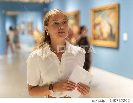 Young girl holding an information booklet looks at paintings in an art exhibition in museum 140785206