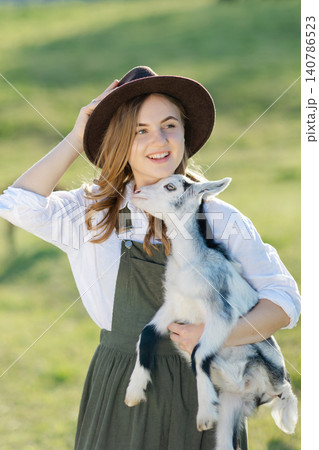 Farmer holding a baby goat in a green field Farmer holding a baby goat in a green field 140786523