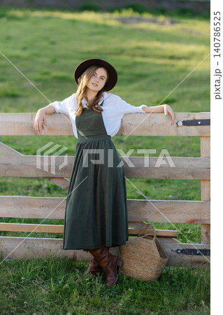 Farmer leaning on wooden fence holding wicker basket in green field Farmer leaning on wooden fence holding wicker basket in green field 140786525