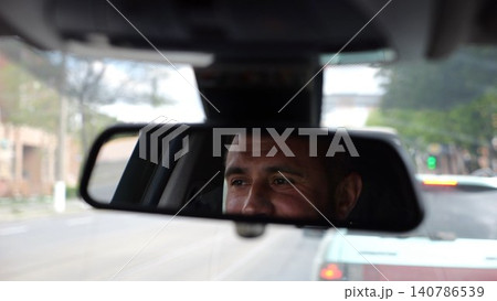 Eyes of male smiling driver reflecting in rearview mirror while riding motor auto. Young man looking concentrated to urban road during operating vehicle. Confident guy driving modern car at city Eyes of male smiling driver reflecting in rearview mirror while riding motor auto. Young man looking concentrated to urban road during operating vehicle. Confident guy driving modern car at city 140786539