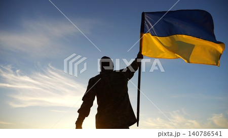 Silhouette of male military lifting blue-yellow banner in honor of the victory against russian aggression at sunset. Soldier of ukrainian army raised a waving flag of Ukraine at countryside. Slow mo Silhouette of male military lifting blue-yellow banner in honor of the victory against russian aggression at sunset. Soldier of ukrainian army raised a waving flag of Ukraine at countryside. Slow mo 140786541