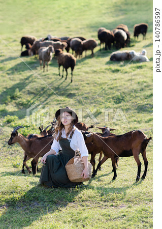 Young farmer feeding goats in green field with goats in background 140786597