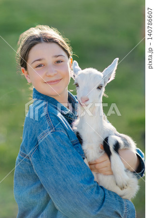 Teenager farmer girl holding baby goat in green field Teenager farmer girl holding baby goat in green field 140786607